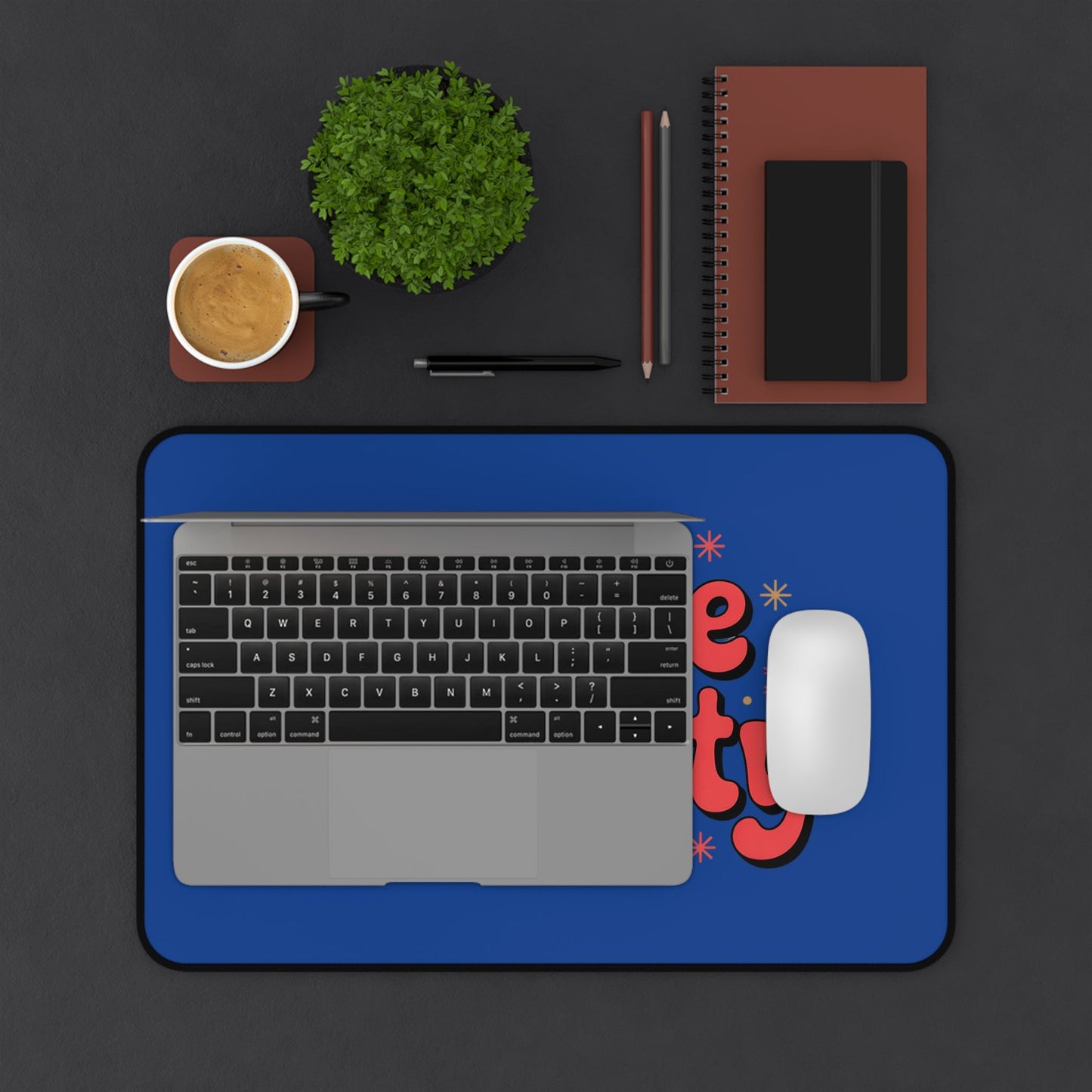 Define Naughty Desk Mat with bold blue background and playful red text, shown with laptop and mouse on a black desk surface.