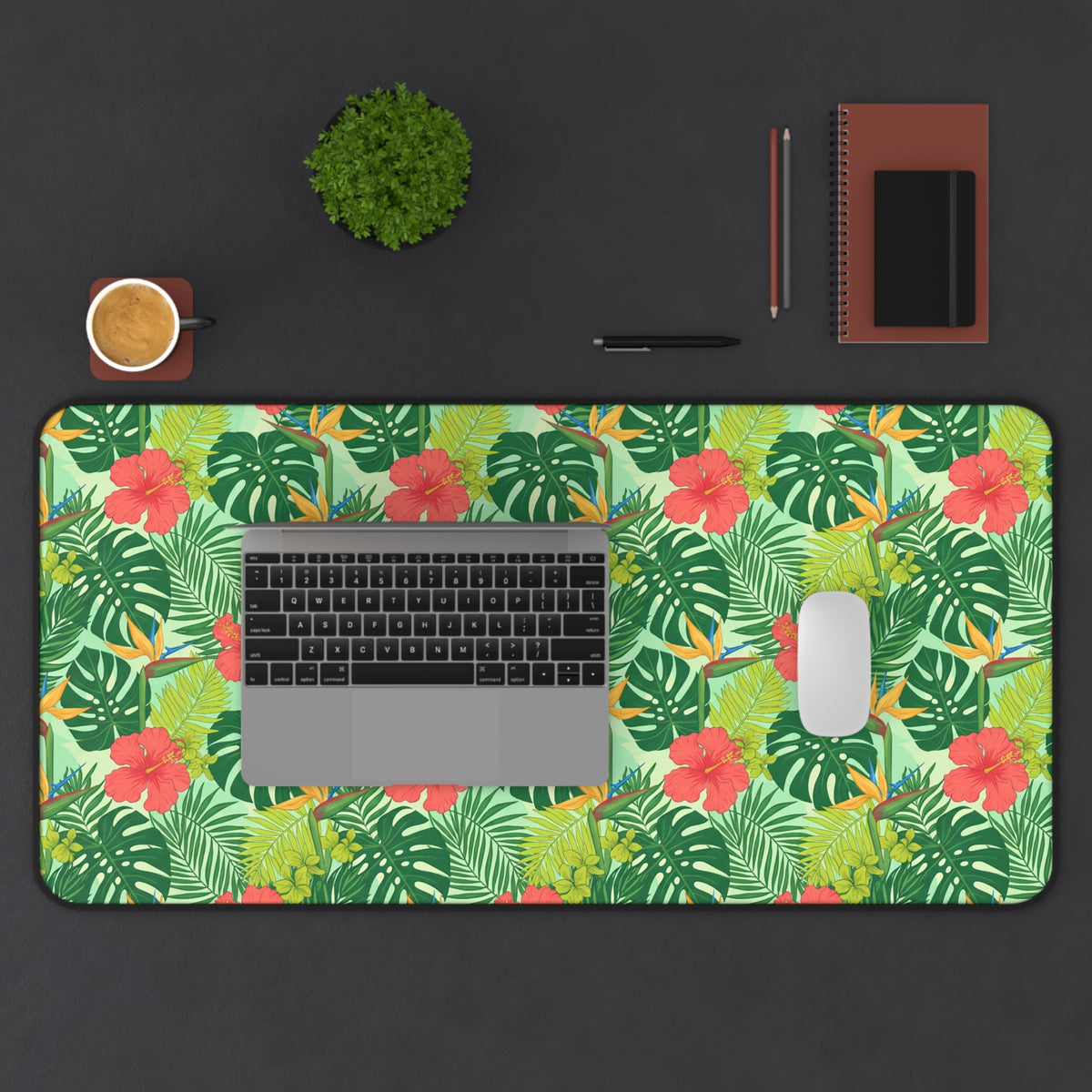 Tropical floral and leaf pattern desk mat with laptop, mouse, and coffee cup.