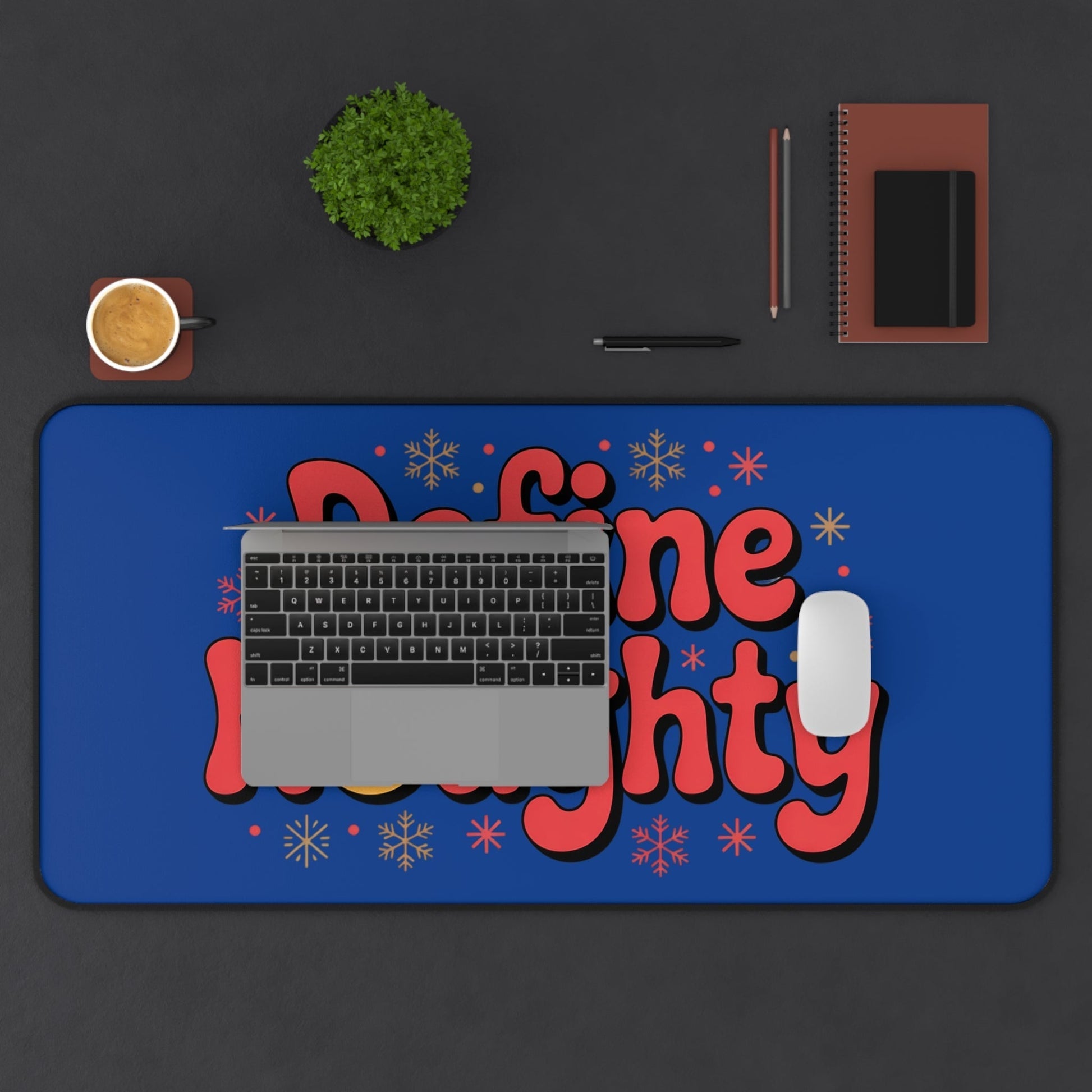 Define Naughty Desk Mat with vibrant blue background and bold red text on office desk with laptop, mouse, notebook, pen, coffee cup, and small plant.
