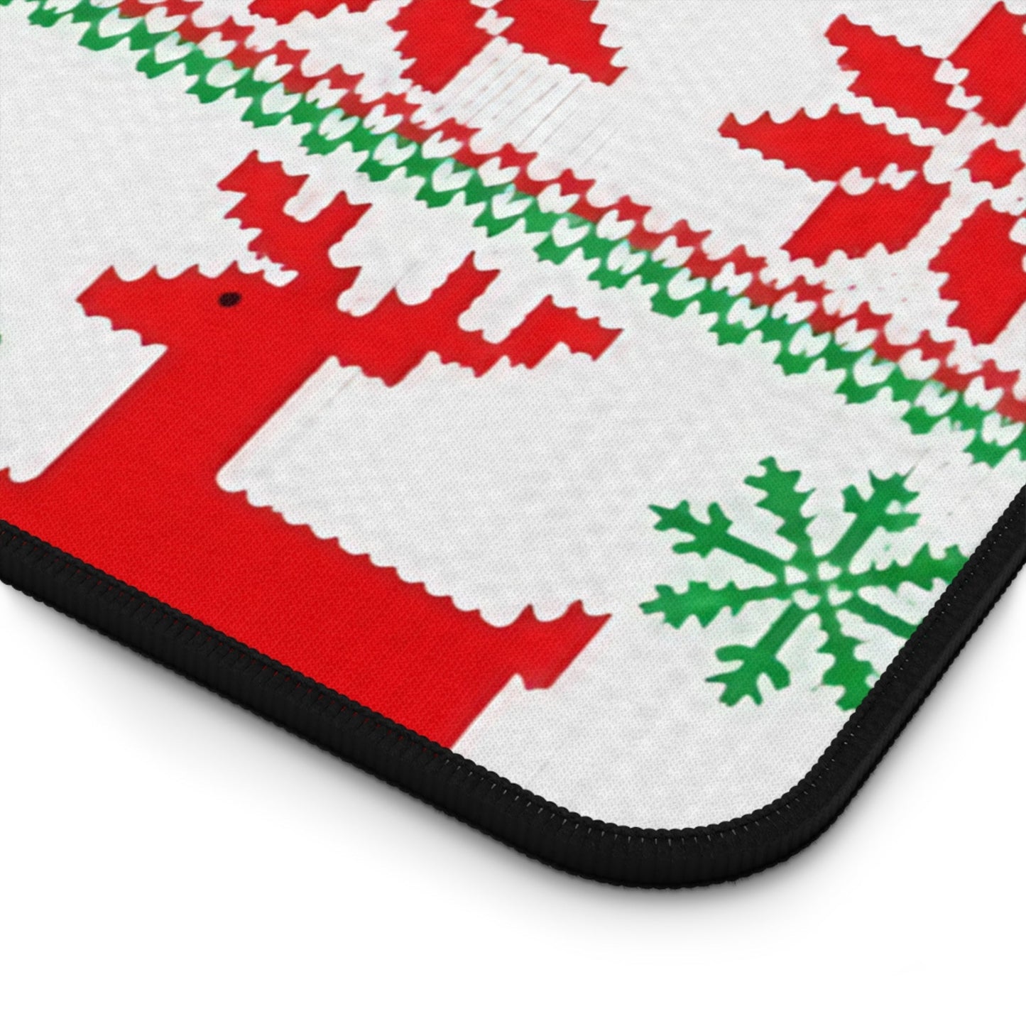 Close-up of ugly sweater inspired desk mat with red, green, and white festive pattern and black hemmed edges