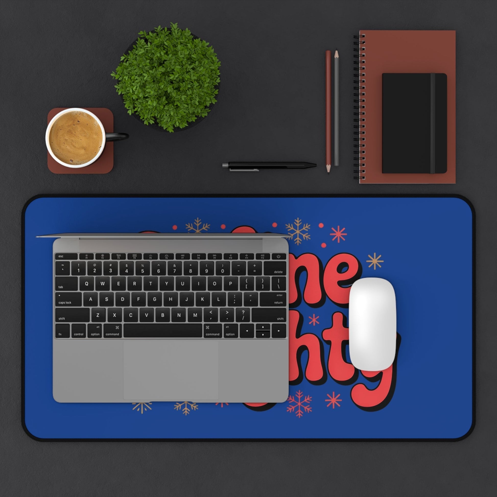 Define Naughty Desk Mat in vibrant blue with red lettering on a workspace with laptop, mouse, coffee cup, plant, and notebooks.