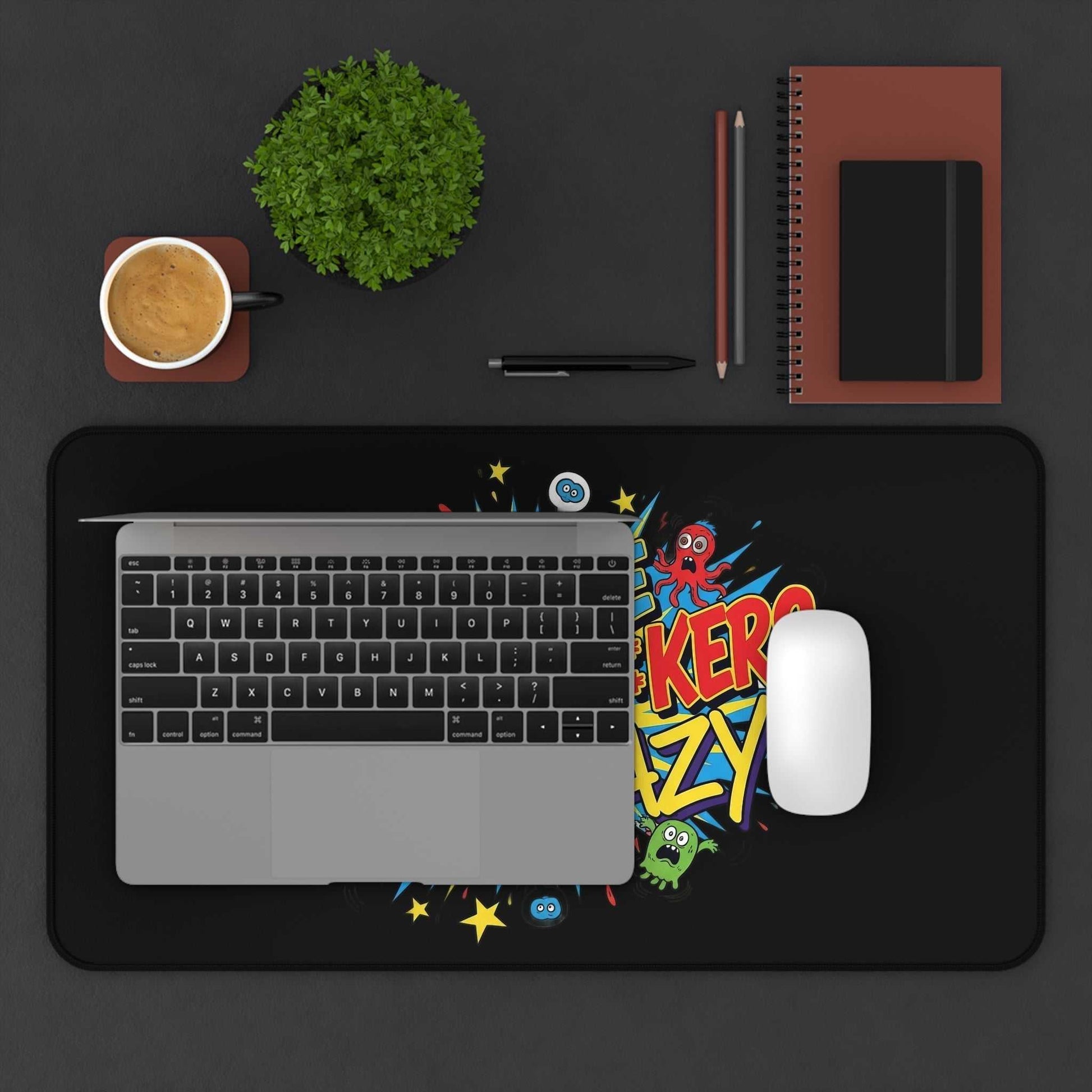 Black desk pad with colorful "These Motherf++kers Are Crazy" text, laptop, mouse, coffee cup, and office supplies on a dark surface