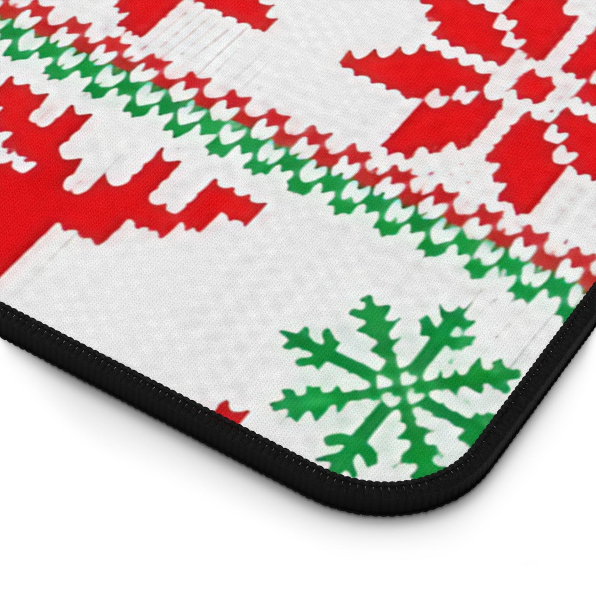 Close-up of Ugly Sweater Inspired Desk Mat with festive red and green Christmas pattern and black hemmed edges