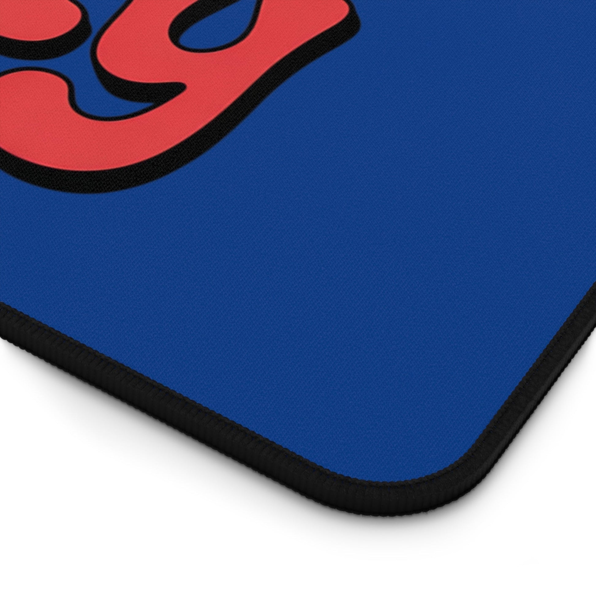 Corner of a blue Define Naughty Desk Mat with red and black playful design and black hemmed edges.