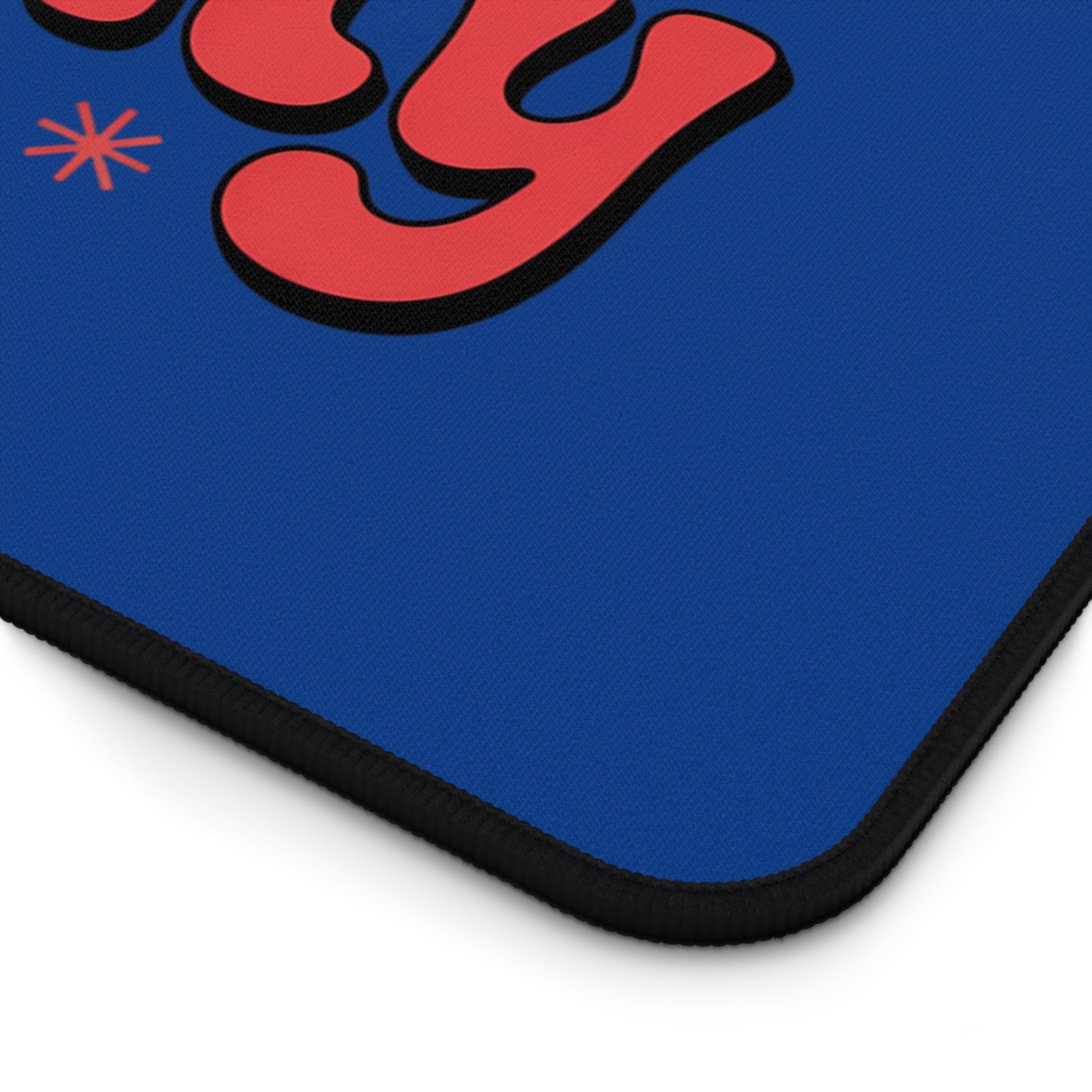 Close-up of Define Naughty Desk Mat corner showing blue surface with red lettering and black hemmed edges