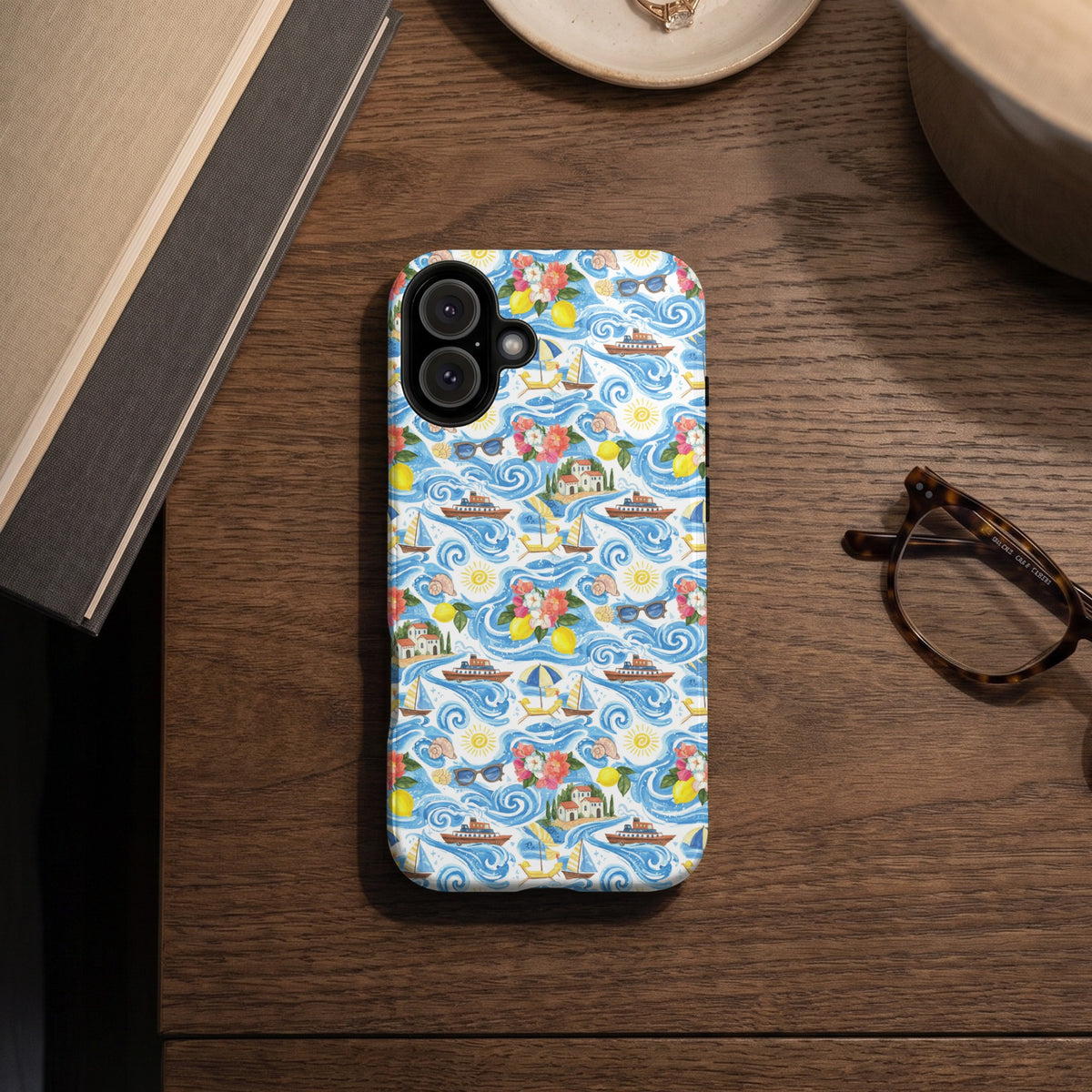 Phone case with a watercolor pattern of boats, lemons, houses, and flowers on a blue wavy background.